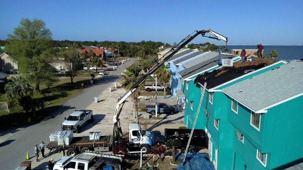 Aerial view of a crane delivering roofing materials to coastal townhomes under replacement