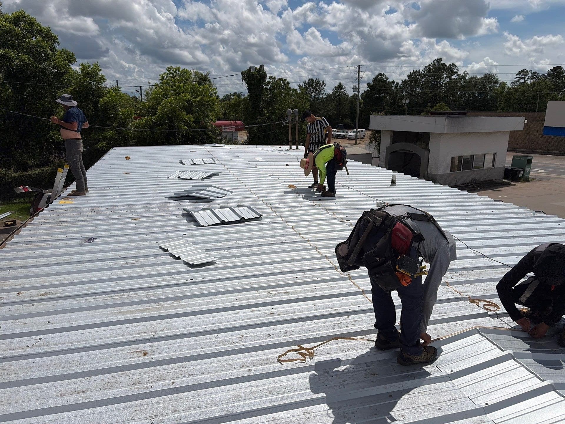 Crew fastening new metal roof panels on a commercial building